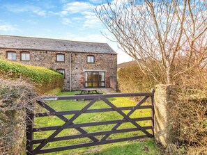 A stone building with a wooden gate, a grassy yard, and a clear sky. - Barley Store - UK48910 (Allonby)