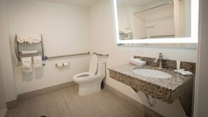 Une salle de bain moderne avec des toilettes, un lavabo et un miroir. On y trouve des serviettes et un sèche-mains fixés au mur.