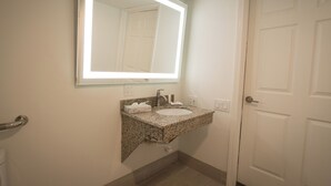 Une salle de bain avec un lavabo doté d’un plan de travail en granit, un miroir et une porte blanche.