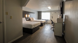 A hotel room with two beds, a desk, a chair, a refrigerator, and a window with curtains.