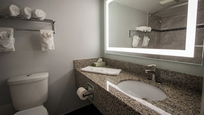 A bathroom with a toilet, sink, and mirror. There are towels on a rack and a tissue box on the counter.