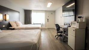 A hotel room with two beds, a desk with a chair, a microwave, and a television.