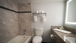 A modern bathroom with a bathtub, toilet, and granite countertop.