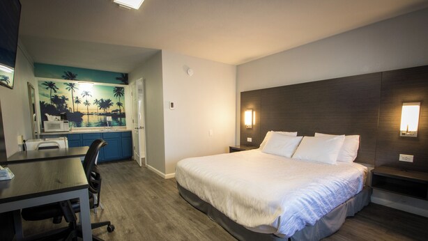 A hotel room with a bed, desk, chair, and a view of a beach mural. - King Accessible Non-Smoking Pet Friendly (Henderson)
