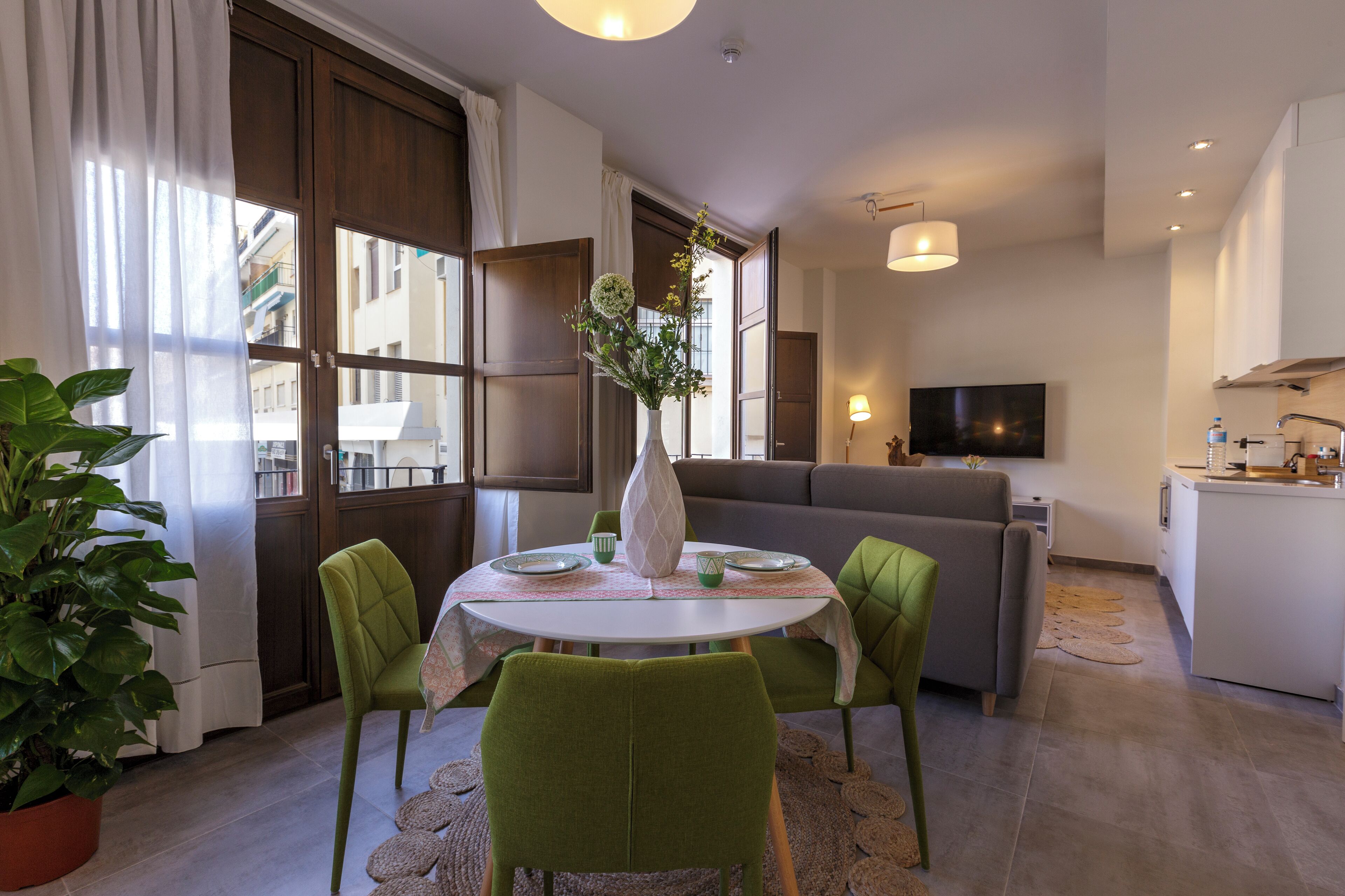 Un salon moderne comprenant une table à manger, des chaises vertes, un canapé gris, un téléviseur à écran plat et un coin cuisine.