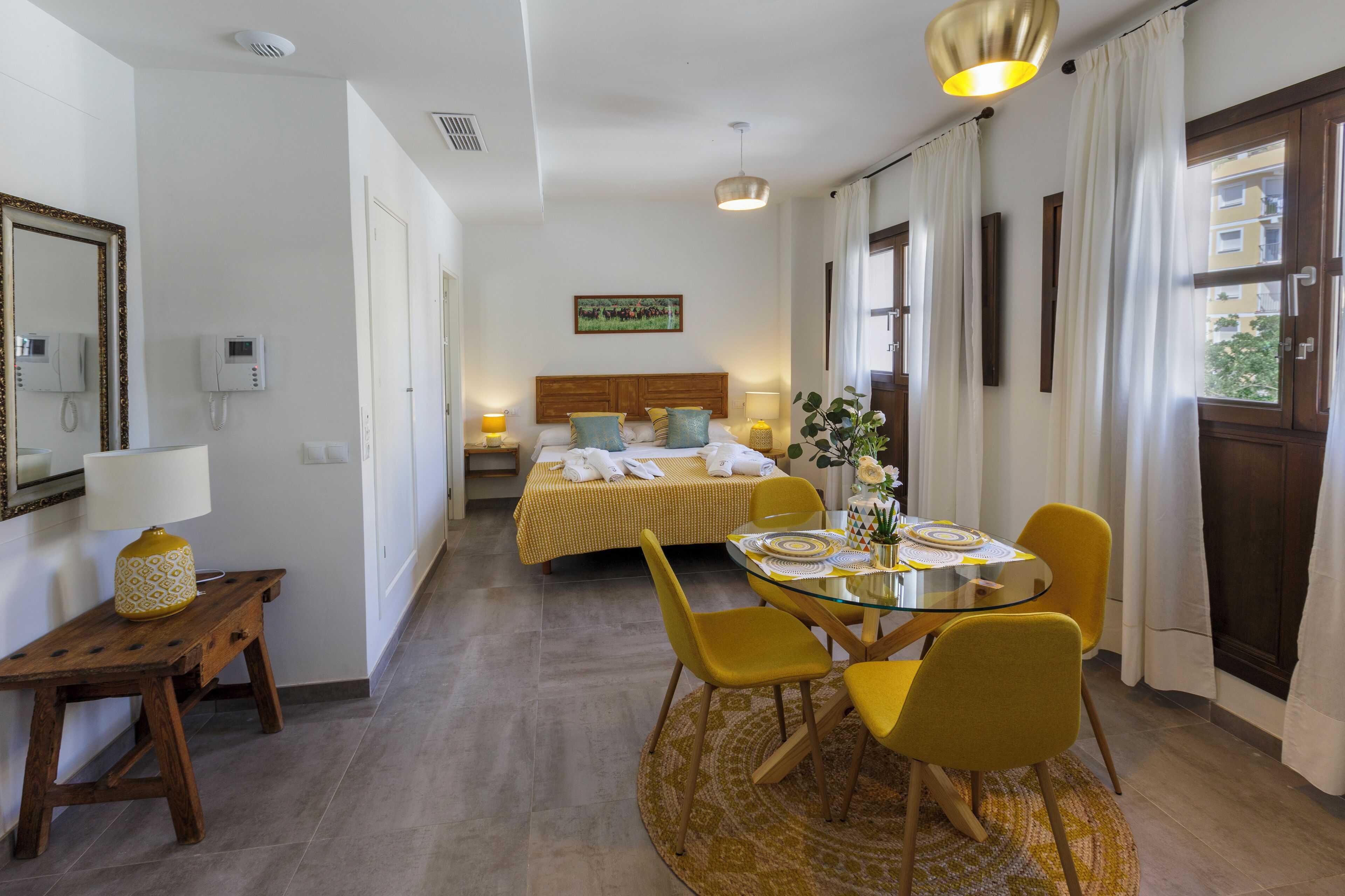 Una habitación de hotel con cama, mesita de noche, lámpara y un comedor con sillas y mesa.