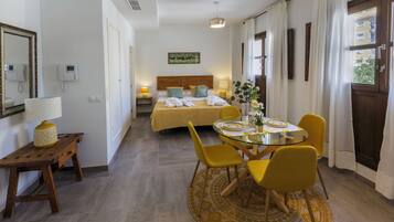 A hotel room with a bed, bedside table, lamp, and a dining area with chairs and a table.