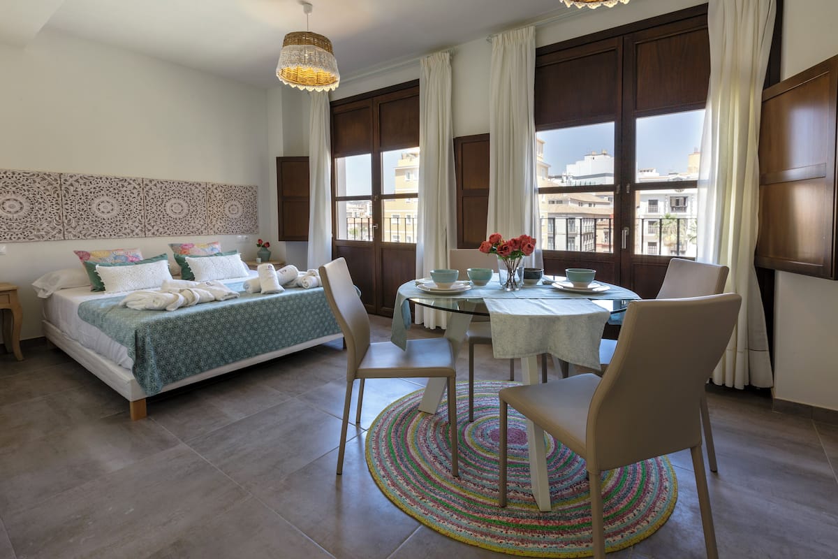 A bedroom with a bed, bedside table, and a view of the city through large windows.