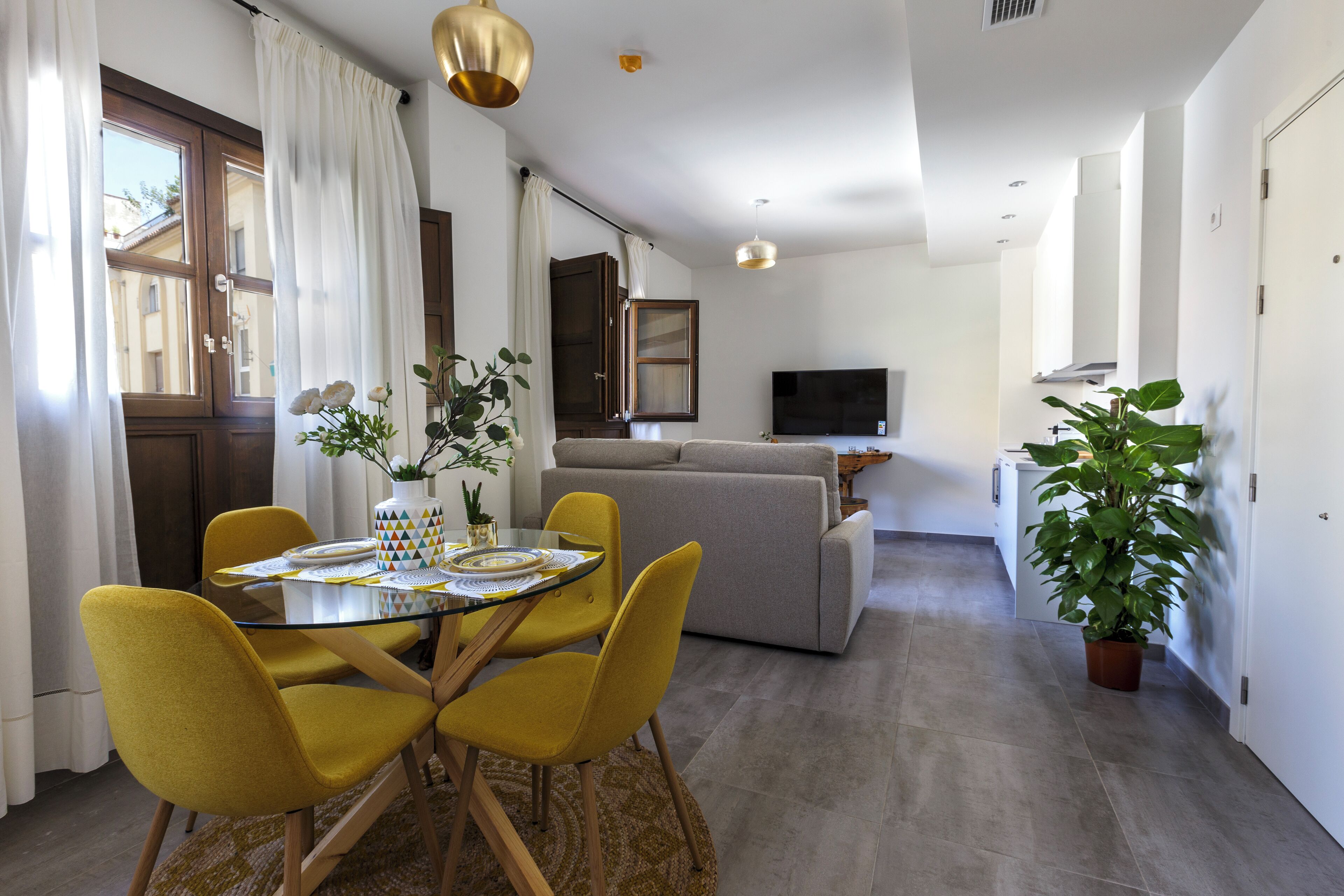 A modern living room with a sofa, a dining table with yellow chairs, and a TV.