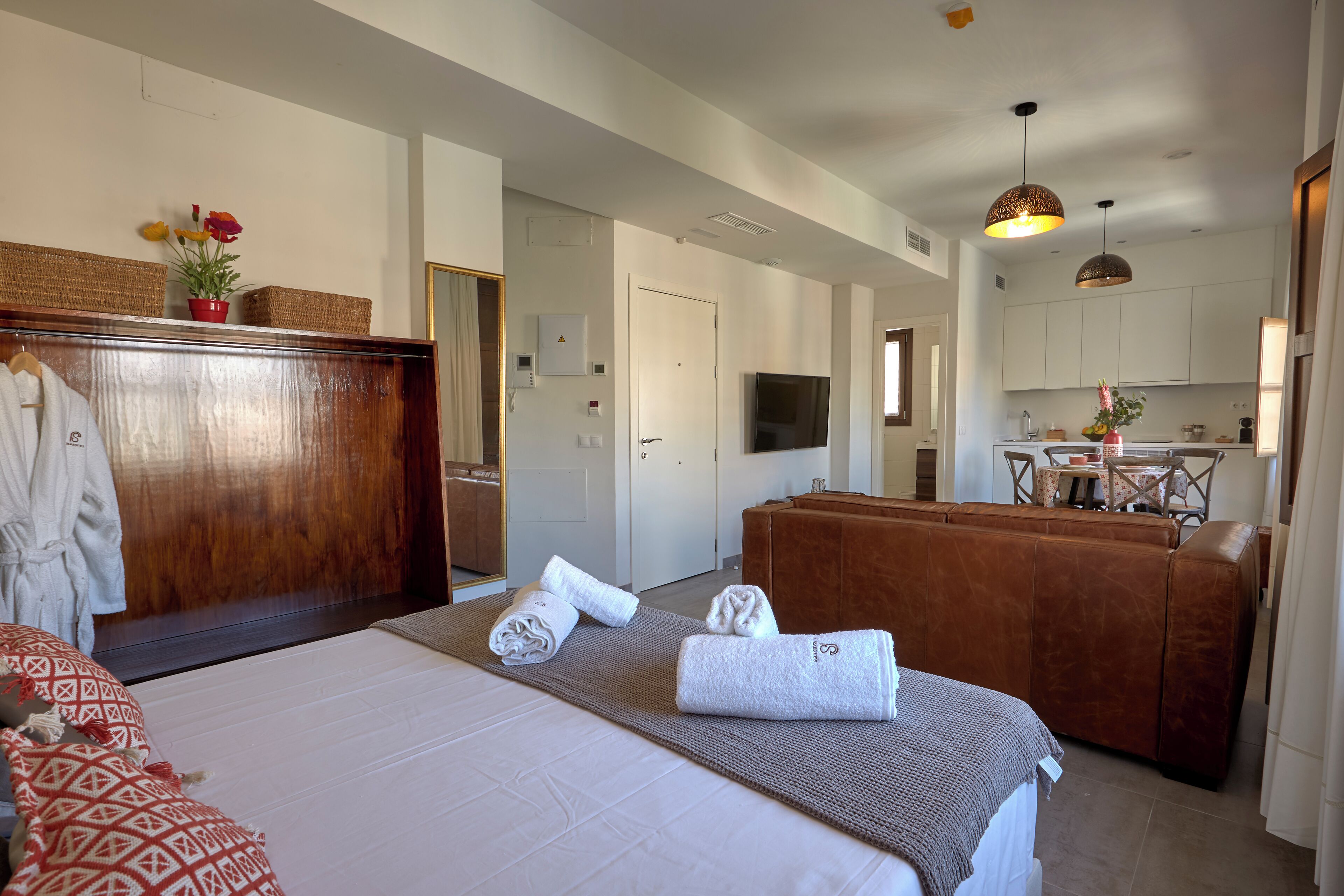 Ein Hotelzimmer mit Bett, Holzschrank, Bad, Küchenzeile und Essbereich.