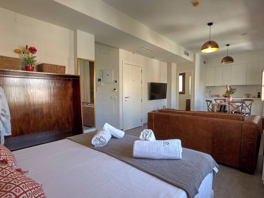 Ein Hotelzimmer mit Bett, Holzschrank, Bad, Küchenzeile und Essbereich.