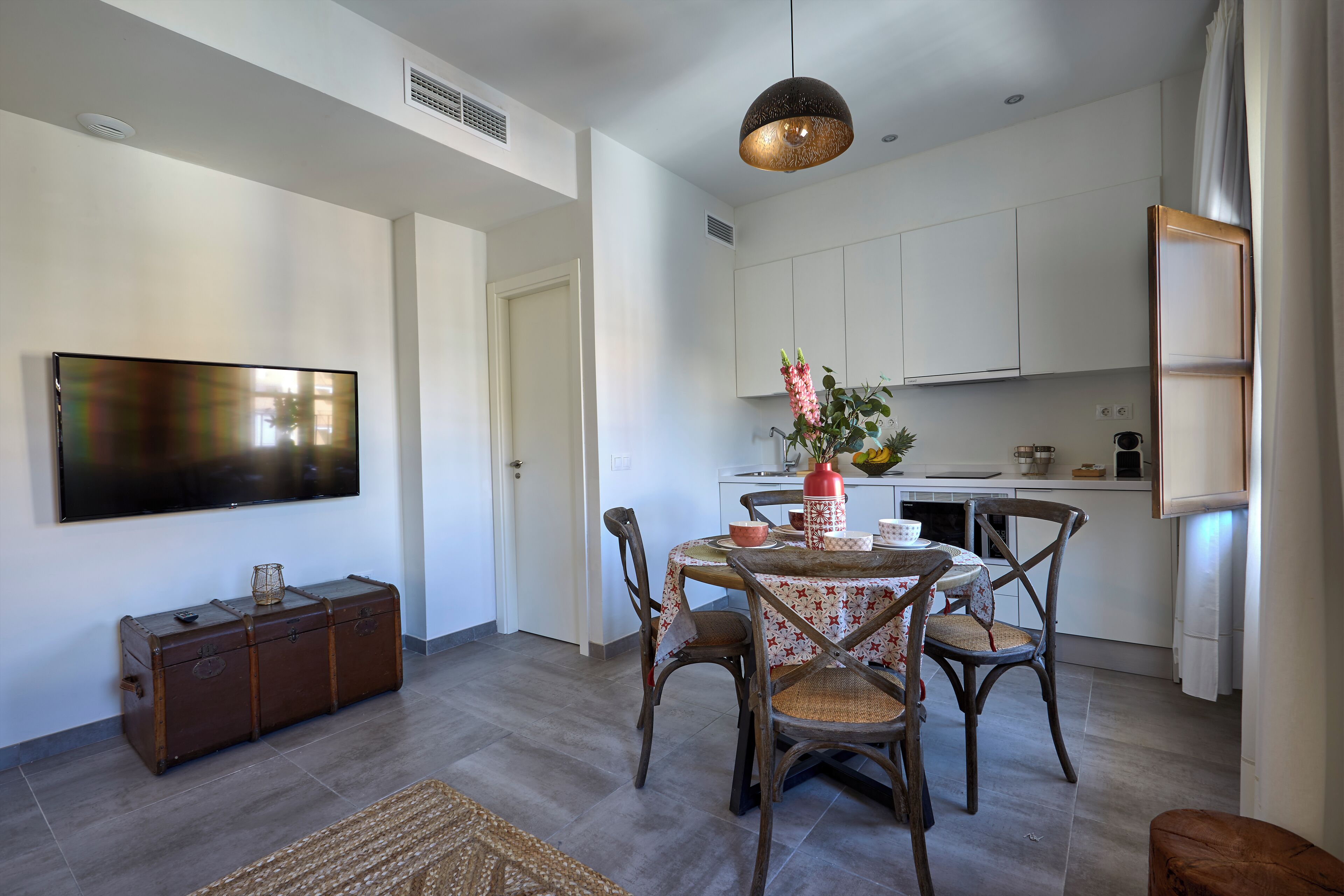A modern kitchen with white cabinets, a dining table with chairs, and a flat-screen TV mounted on the wall.