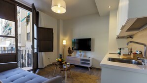 Ein modernes Wohnzimmer mit Sofa, Fernseher, Essbereich mit Tisch und Stühlen sowie Küche mit Spüle und Arbeitsfläche.