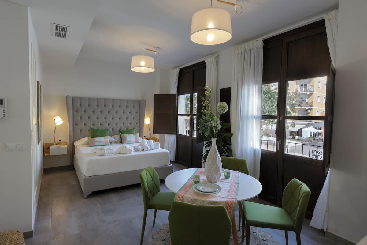 A bedroom with a bed, bedside table, lamp, and a view of the outside.