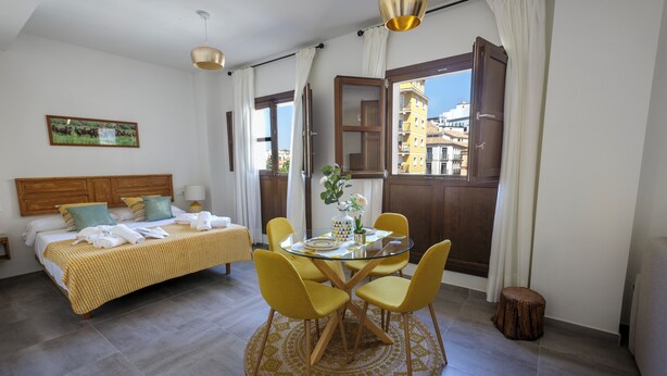 Ein Hotelzimmer mit einem Bett, einem runden Esstisch mit Stühlen, einem kleinen Hocker und einem Fenster mit Vorhängen.