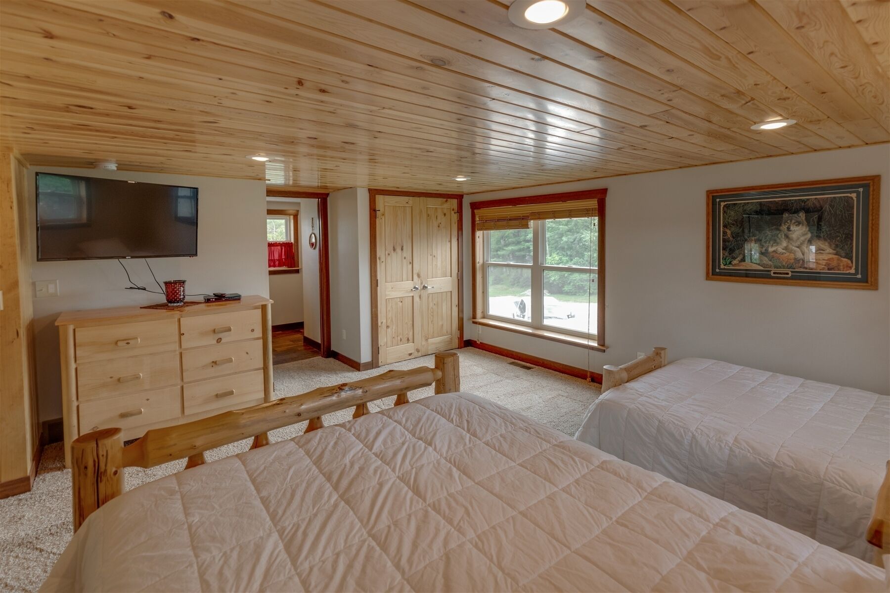 A bedroom with two beds, a wooden dresser, a TV, and a window with a view of trees.