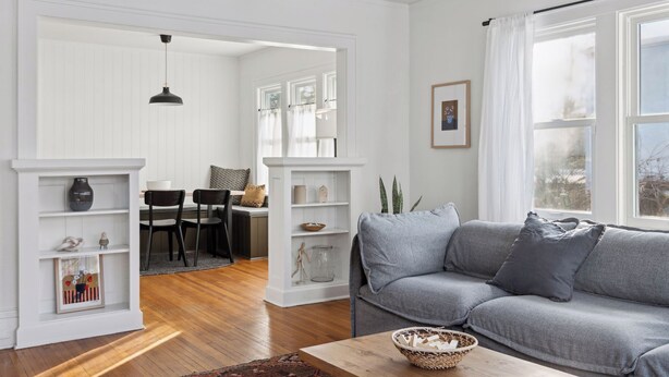 A modern living room with a grey sofa, wooden flooring, white walls, and a dining area with a table and chairs. - Linden Hills Edina. Remolded Home Near the Lakes. King Bed. Sleeps 10. (Minneapolis)