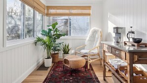 A cozy room with a large window, a white chair, a coffee maker, and a wooden side table. - Linden Hills Edina. Remolded Home Near the Lakes. King Bed. Sleeps 10. (Minneapolis)