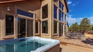 Ein modernes Haus mit Whirlpool auf der Terrasse, großen Fenstern und einer Terrasse mit Gartenmöbeln.