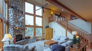 A cozy living room with a stone fireplace, a staircase, and a large window. - Zion Views- La Mesa Lodge + Resort Access (Orderville)