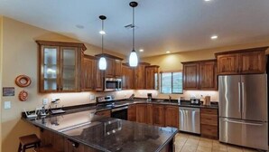A spacious kitchen with wooden cabinets, a large island, stainless steel appliances, and pendant lighting.