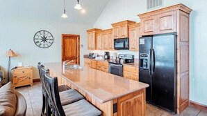 A kitchen with wooden cabinets, a black refrigerator, a microwave, and a large island with seating.