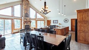 A spacious kitchen with a stone fireplace, large windows, and a dining area with wooden furniture.