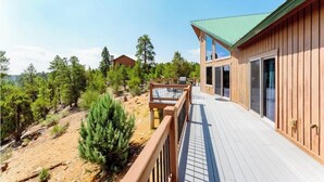 A wooden cabin with a deck, surrounded by trees and a clear sky.