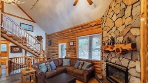 A log cabin interior with a wooden staircase, a stone fireplace, a leather sofa, and a dining table. - Zion Views- The Ranch House +Resort Access (Orderville)