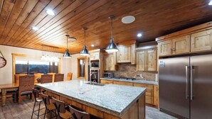 A kitchen with wooden cabinets, a large island with bar stools, stainless steel appliances, and pendant lighting.