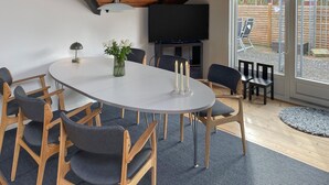 A modern dining area with a round table, wooden chairs, a vase with flowers, and a flat-screen TV mounted on the wall. - 3 bedroom nice home in Væggerløse (Væggerløse)