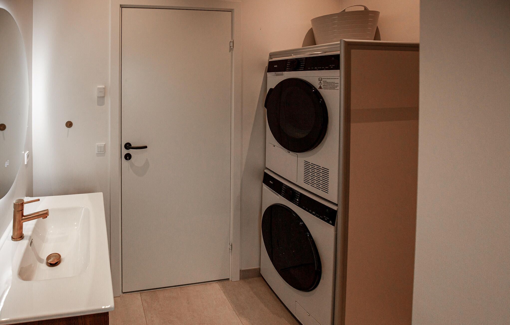A laundry room with a washing machine and dryer, a sink with a copper faucet, and a door.
