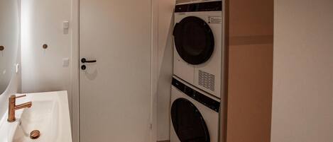 A laundry room with a washing machine and dryer, a sink with a copper faucet, and a door.