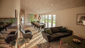 A spacious living area with a large sofa, a dining table, and a coffee table. There is a map on the wall and a large window providing a view of the outdoors. - Amazing home in Hadsund with sauna (Hadsund)