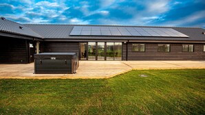 A modern building with a large solar panel array on the roof, a covered outdoor area with a grill, and a grassy yard. - Amazing home in Hadsund with sauna (Hadsund)