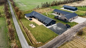 An aerial view of a modern farmhouse with three detached buildings, a large green field, and a winding road. - Amazing home in Hadsund with sauna (Hadsund)