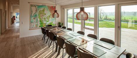 Uma sala de conferência moderna com um mapa grande na parede, uma mesa comprida com cadeiras e amplas janelas que oferecem vista para o exterior.