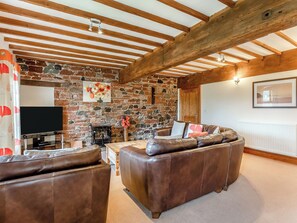 A cozy living room with a stone wall, wooden beams, a fireplace, and leather sofas.