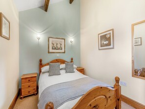 Une chambre à coucher avec un lit en bois, deux tables de chevet, une petite table d’appoint, une lampe fixée au mur et un tableau encadré.