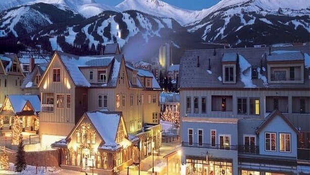 Un pueblo cubierto de nieve con edificios de madera tradicionales y un pico nevado imponente al fondo.