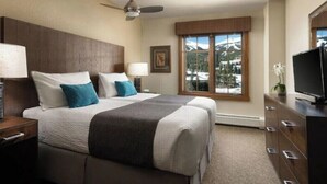 Habitación de hotel con una cama grande, televisión, cómoda y ventana con vista a la montaña.