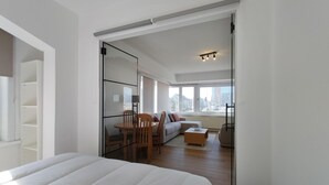 Une chambre moderne avec un grand lit, une porte vitrée donnant sur un espace de vie comprenant un canapé, des fauteuils et une table basse.