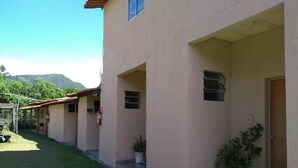 A building with a flat roof, multiple windows, and a door. There is a small garden area with grass and a few potted plants.