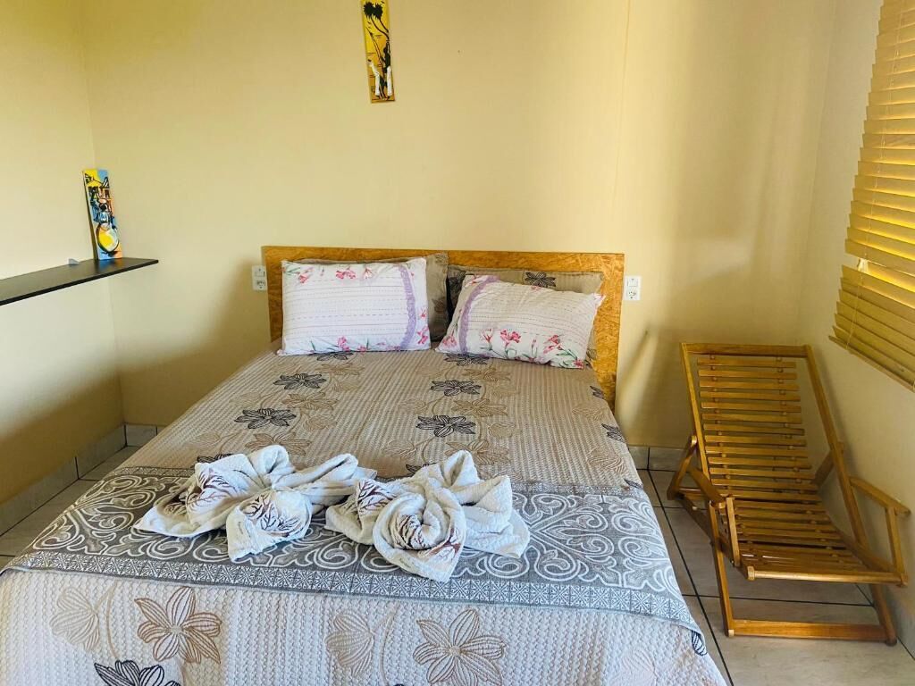 A hotel room with a bed, two pillows, a bedside table, a bench, and a wall with a painting.