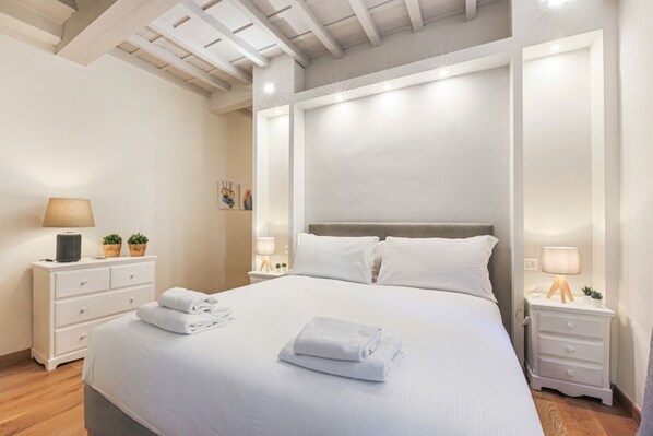 A neatly made bed with white linens and towels, a bedside table with a lamp, and a nightstand with a lamp.