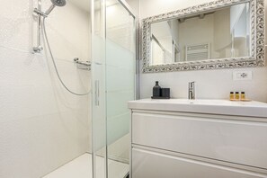 A bathroom with a glass shower enclosure, a white vanity with a mirror, and a sink.