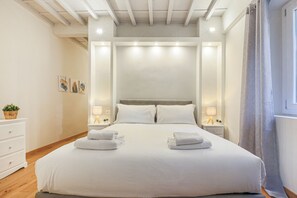 A bedroom with a large bed, two bedside tables with lamps, a white dresser, and a window with curtains.