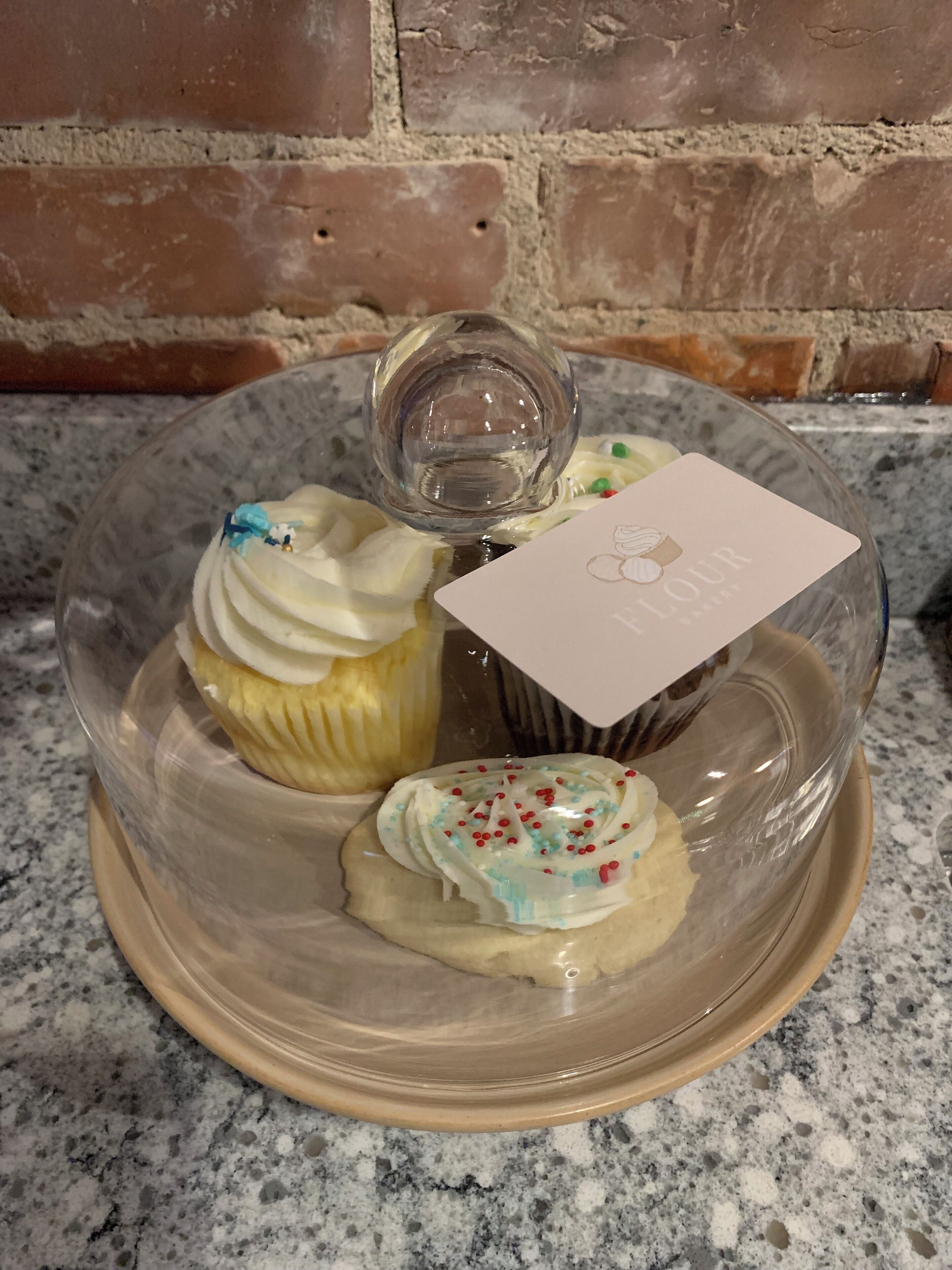 Een glazen vitrine met een taart en een cupcake op een granieten aanrecht.