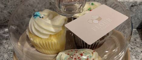 Een glazen vitrine met een taart en een cupcake op een granieten aanrecht.