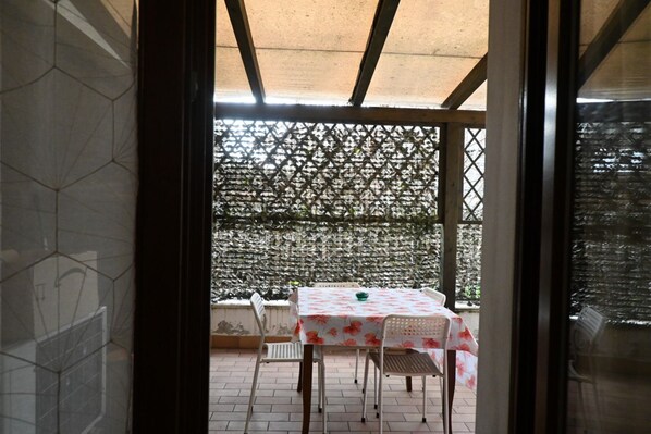 Un patio couvert avec une table et des chaises, une clôture en treillis et une vue sur l’extérieur.